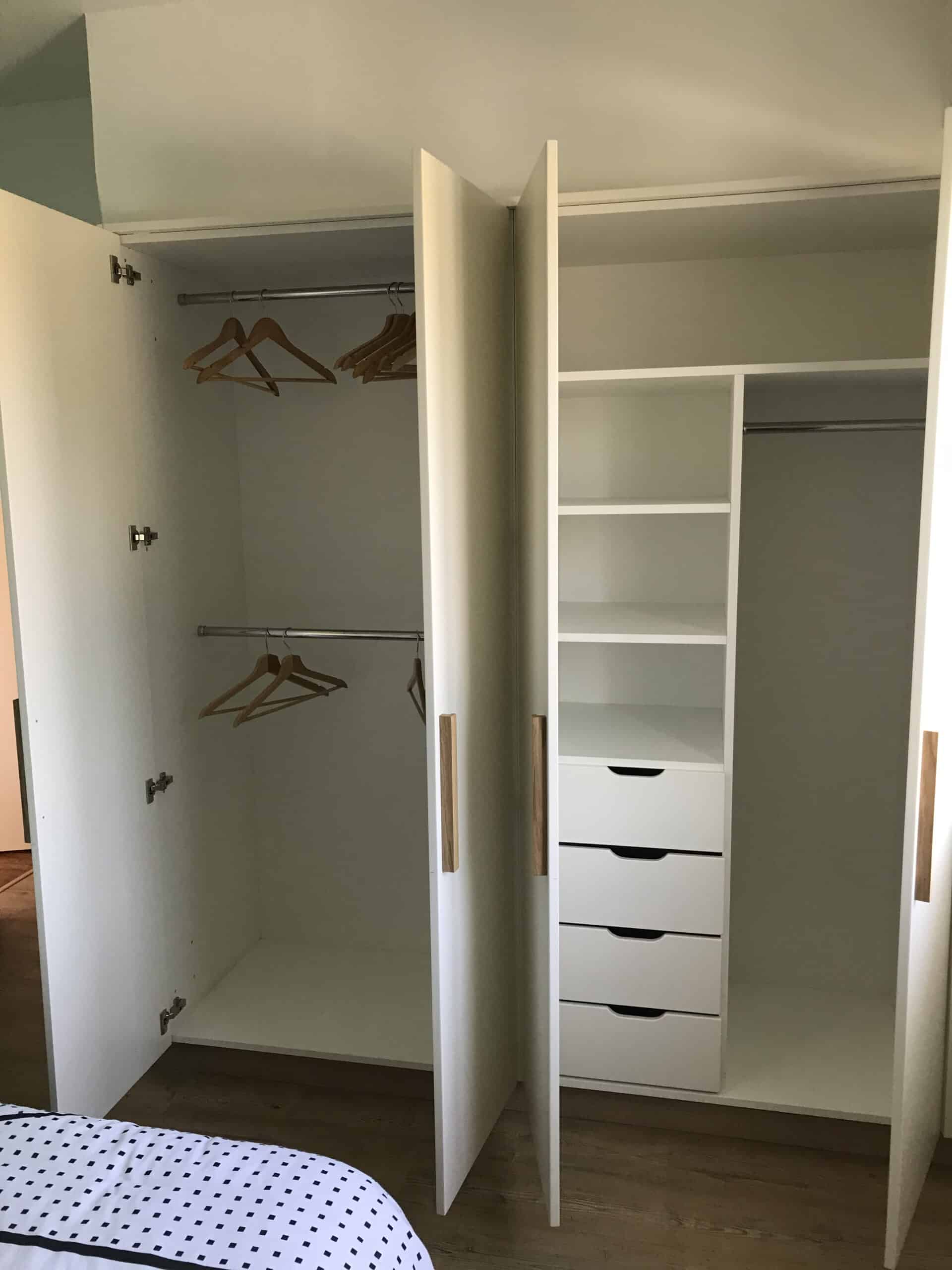 Armoire blanche ouverte avec penderies, cintres en bois, étagères et tiroirs pour une organisation moderne de chambre.