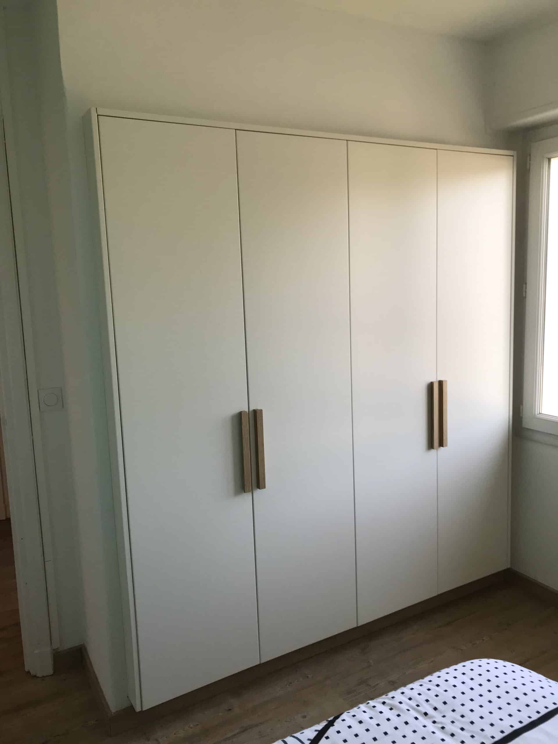 Armoire blanche à quatre portes avec longues poignées en bois clair dans une chambre au design moderne.