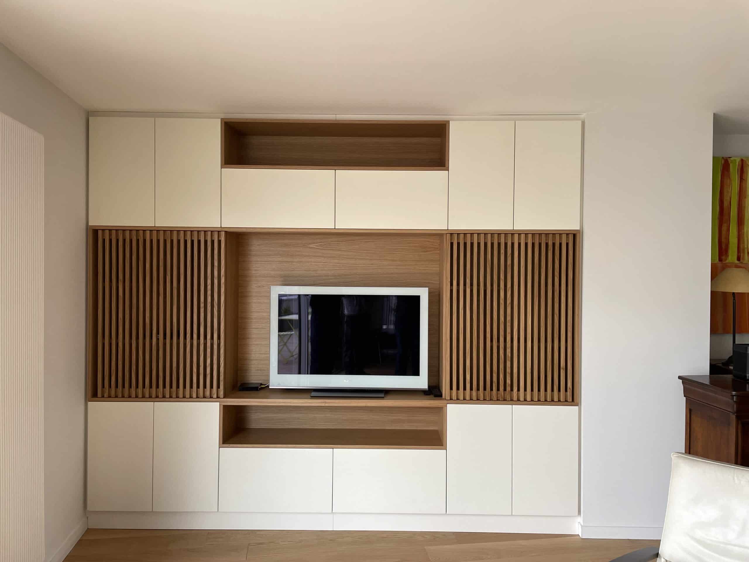 Meuble TV mural moderne en bois clair et blanc avec portes à claire-voie et rangements intégrés dans un salon épuré.