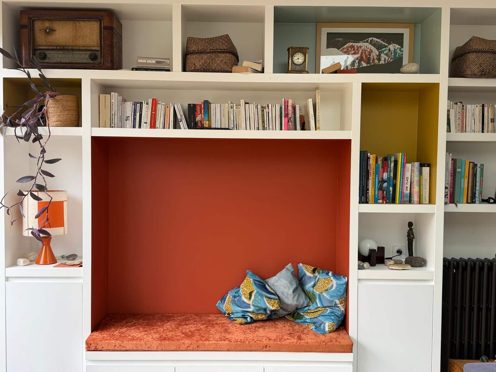 Bibliothèque encastrée avec coin lecture orange, étagères blanches, livres et décoration vintage colorée.