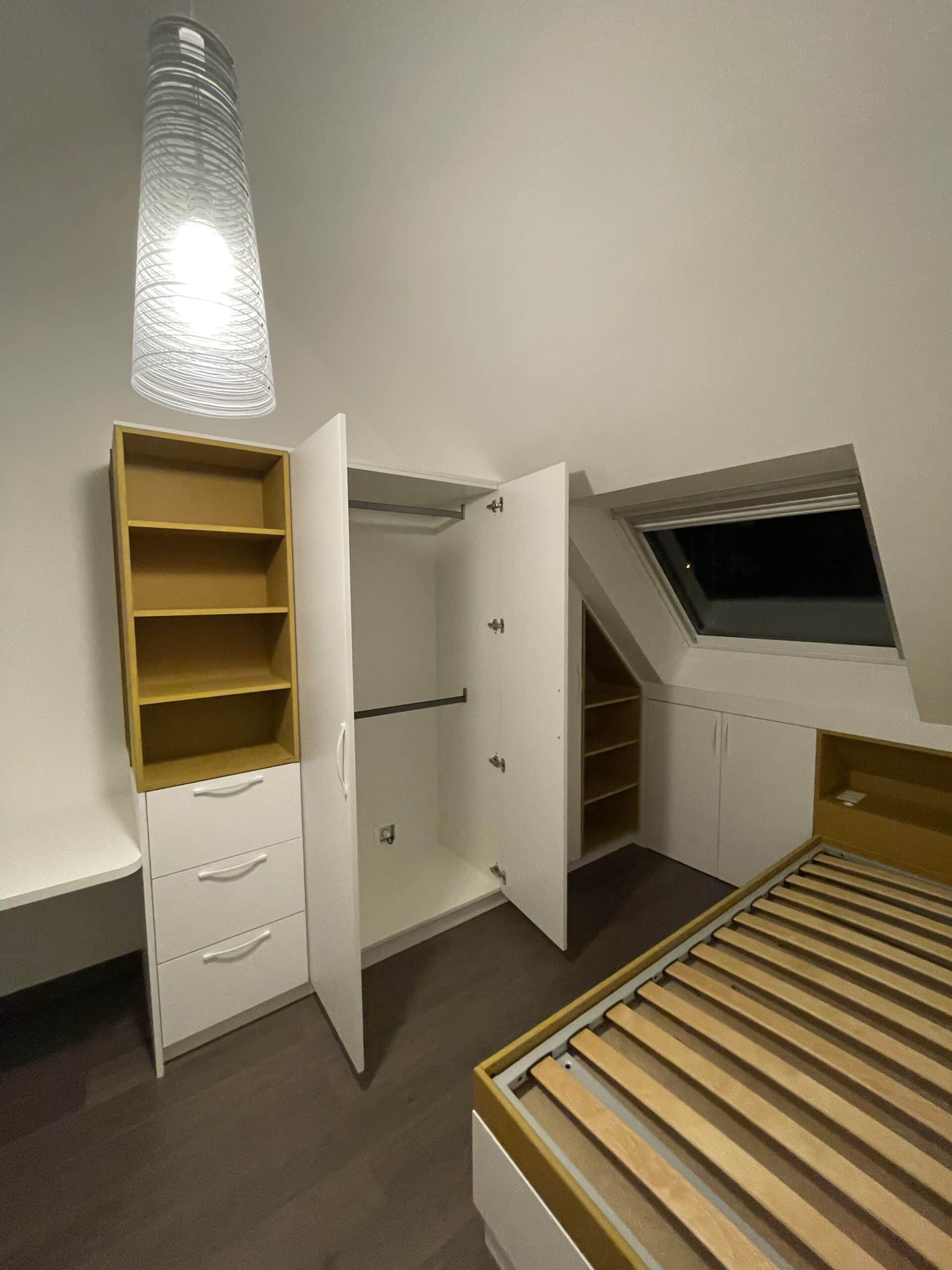 Chambre sous les combles avec placards sur mesure blancs et jaunes, lit à lattes et fenêtre de toit.