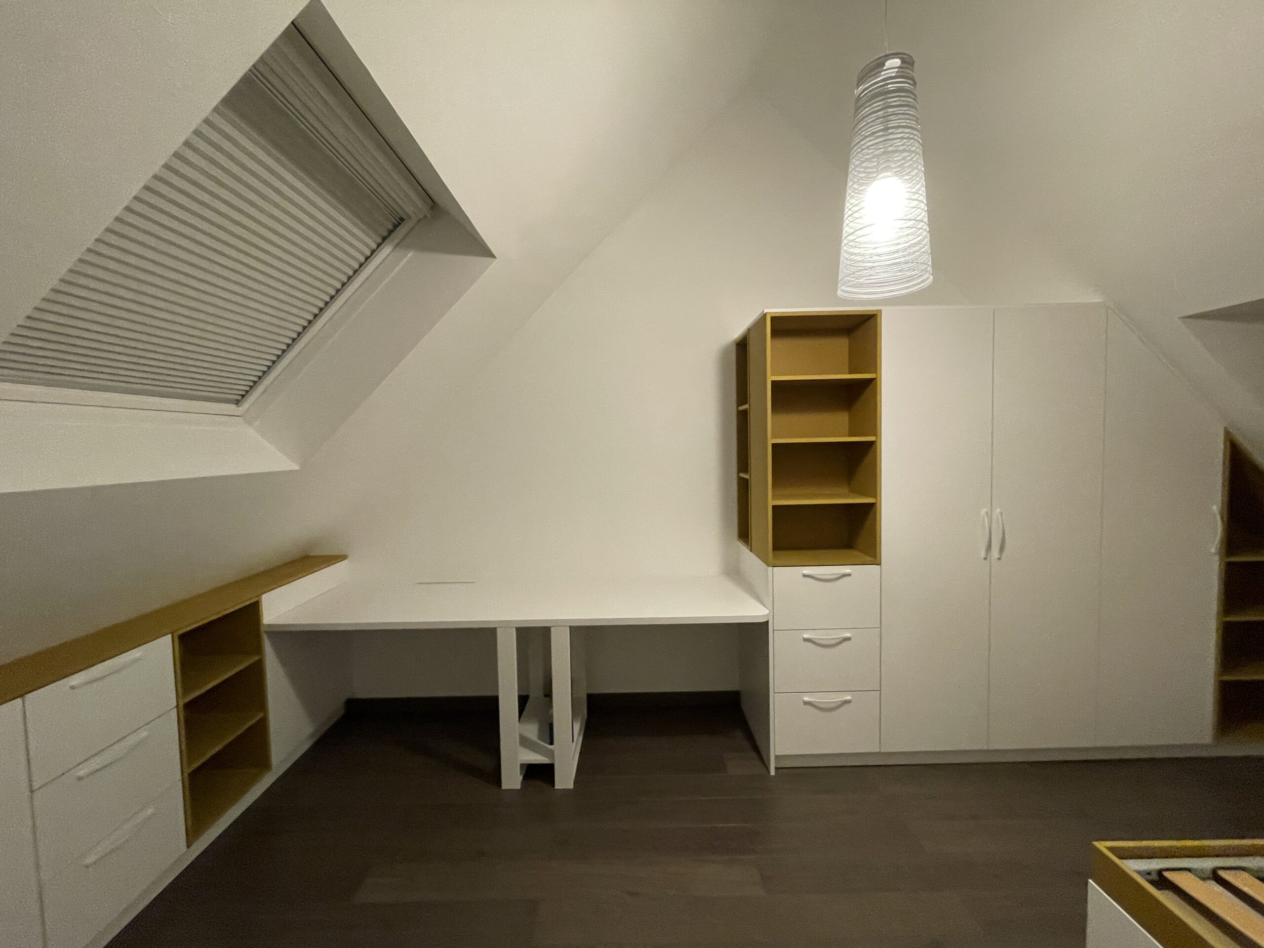 Bureau et rangements blancs et bois sous pente avec velux et luminaire design dans une chambre mansardée.