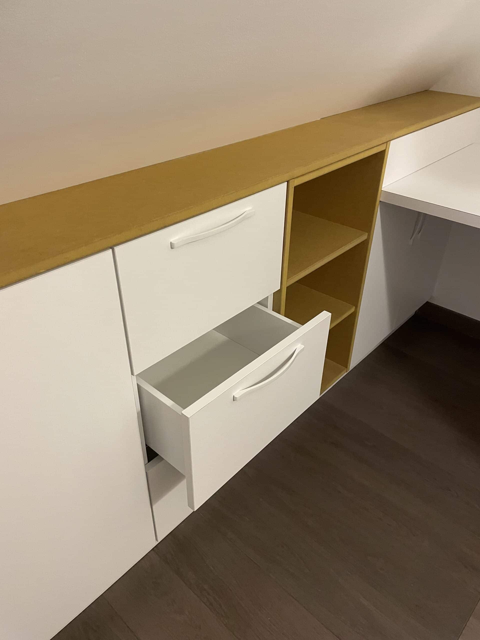 Meuble sur mesure blanc et bois sous pente avec tiroirs ouverts et étagères pour un rangement optimisé.