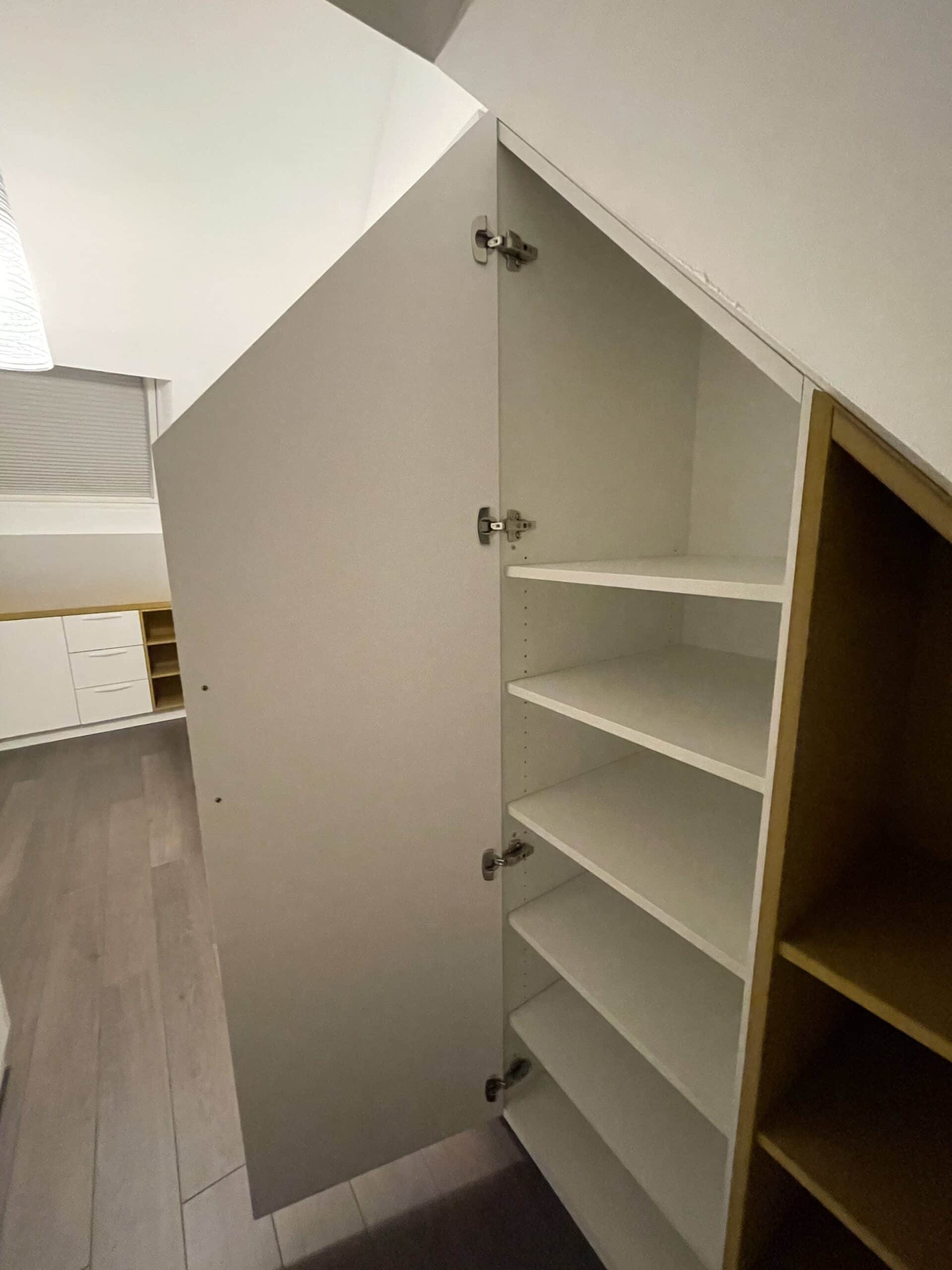Placard blanc sur mesure sous pente avec étagères et porte battante dans une pièce mansardée.