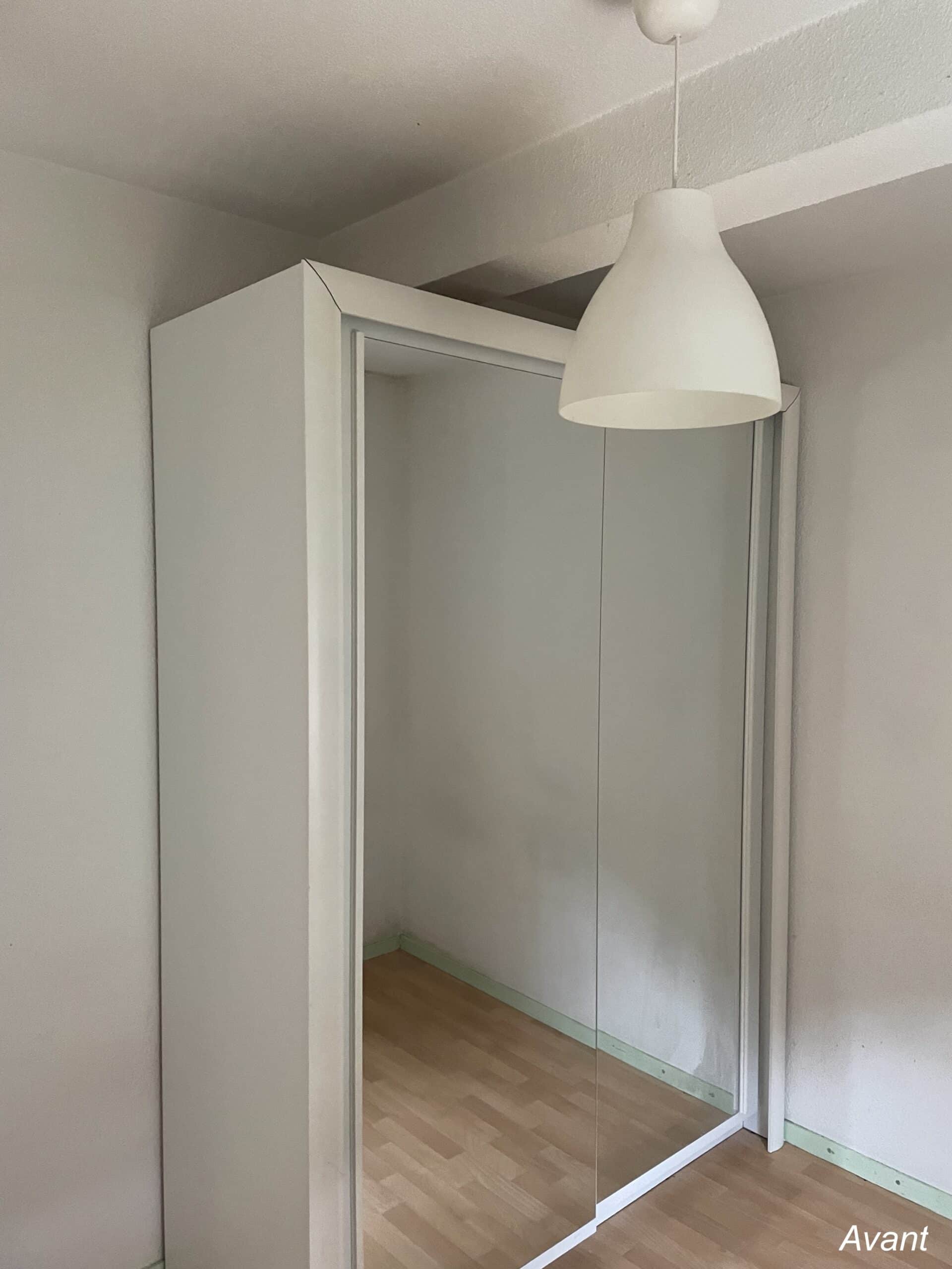Armoire blanche à deux portes miroirs coulissantes sous un luminaire suspendu, texte 'Avant' en bas à droite.