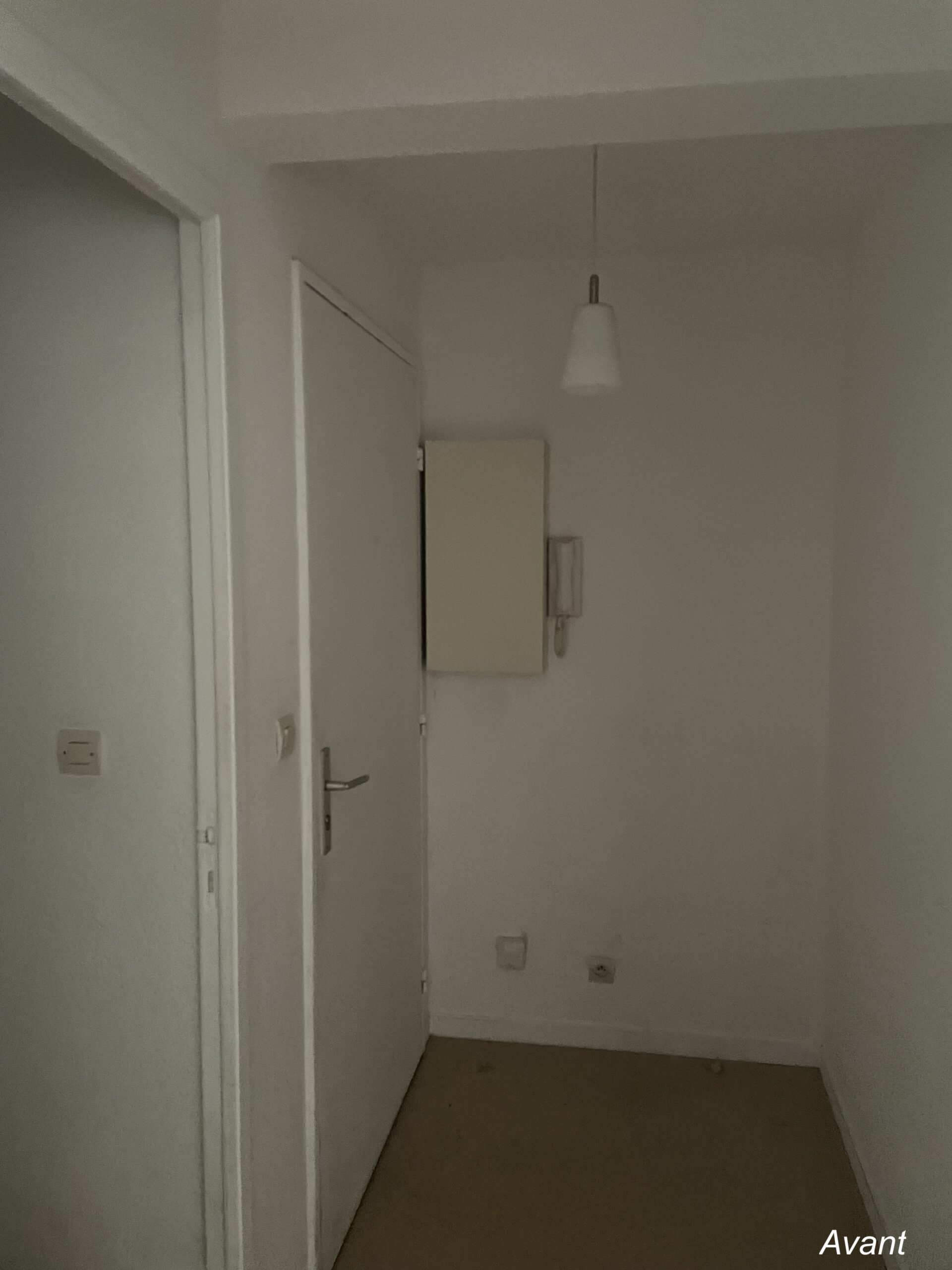 Petit couloir blanc étroit avant rénovation avec porte, luminaire suspendu et tableau électrique. Texte : Avant.