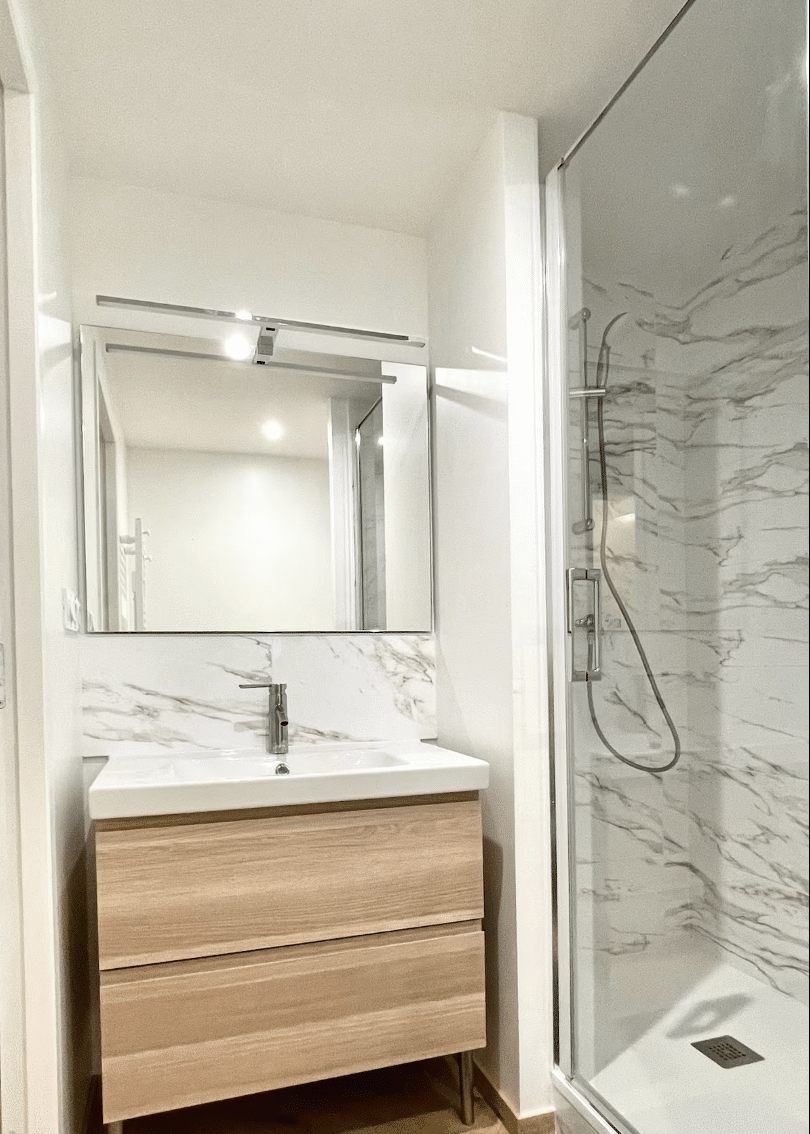 Meuble vasque en bois clair, miroir et douche à l'italienne effet marbre dans une salle de bain moderne lumineuse.
