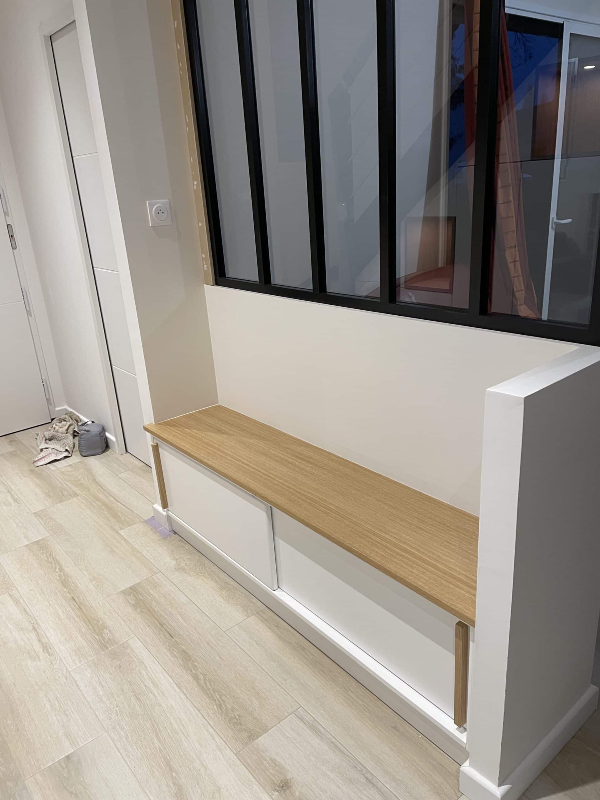 Banquette d'entrée avec assise bois, rangements blancs et verrière de style industriel.