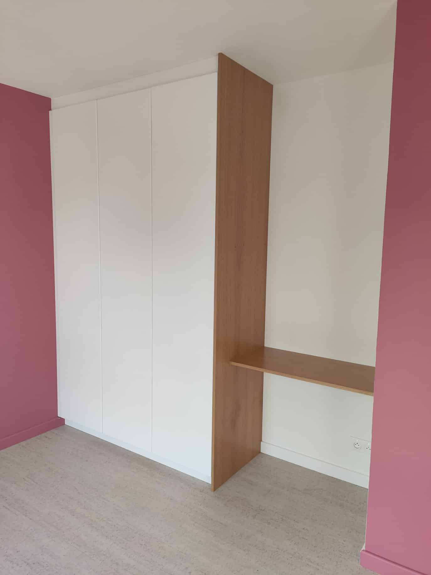 Placard sur mesure blanc avec bureau en bois clair intégré dans une chambre aux murs roses.