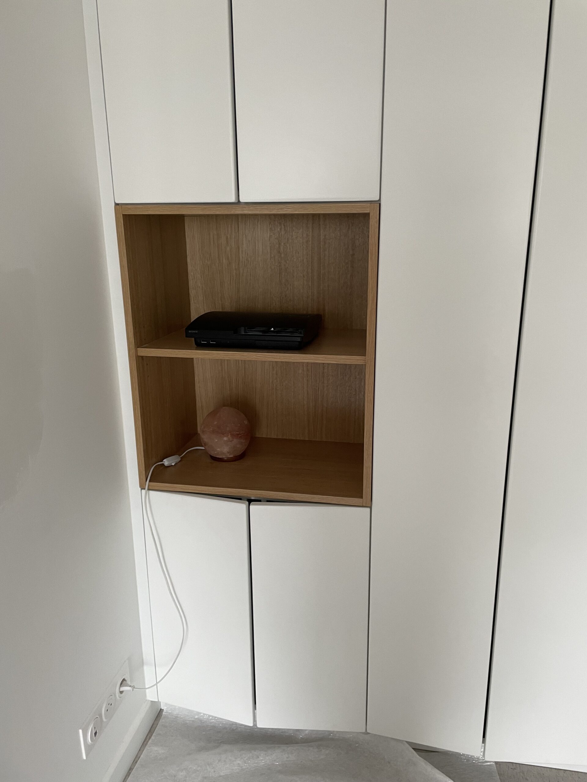 Armoire blanche encastrée avec niche en bois contenant une PS3 Sony et une lampe de sel rose branchée.