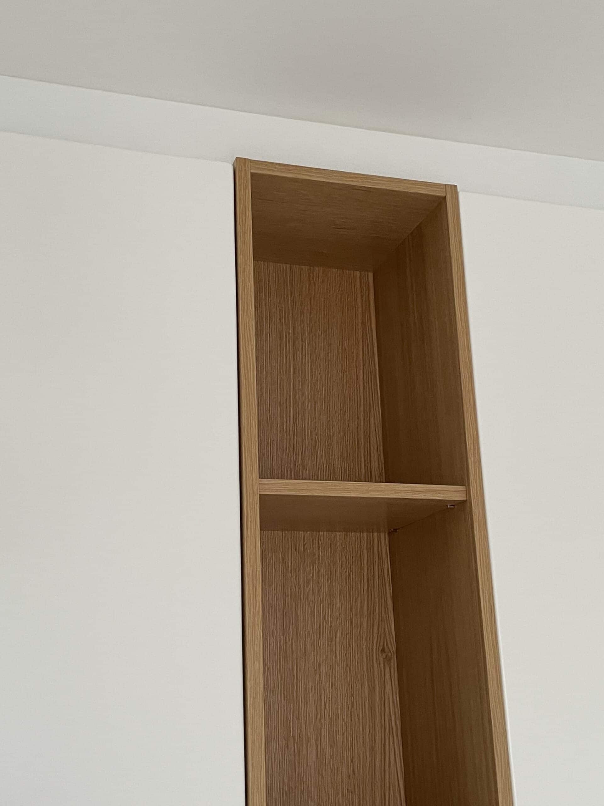 Étagère en bois clair intégrée dans un placard blanc minimaliste avec finitions soignées au plafond.