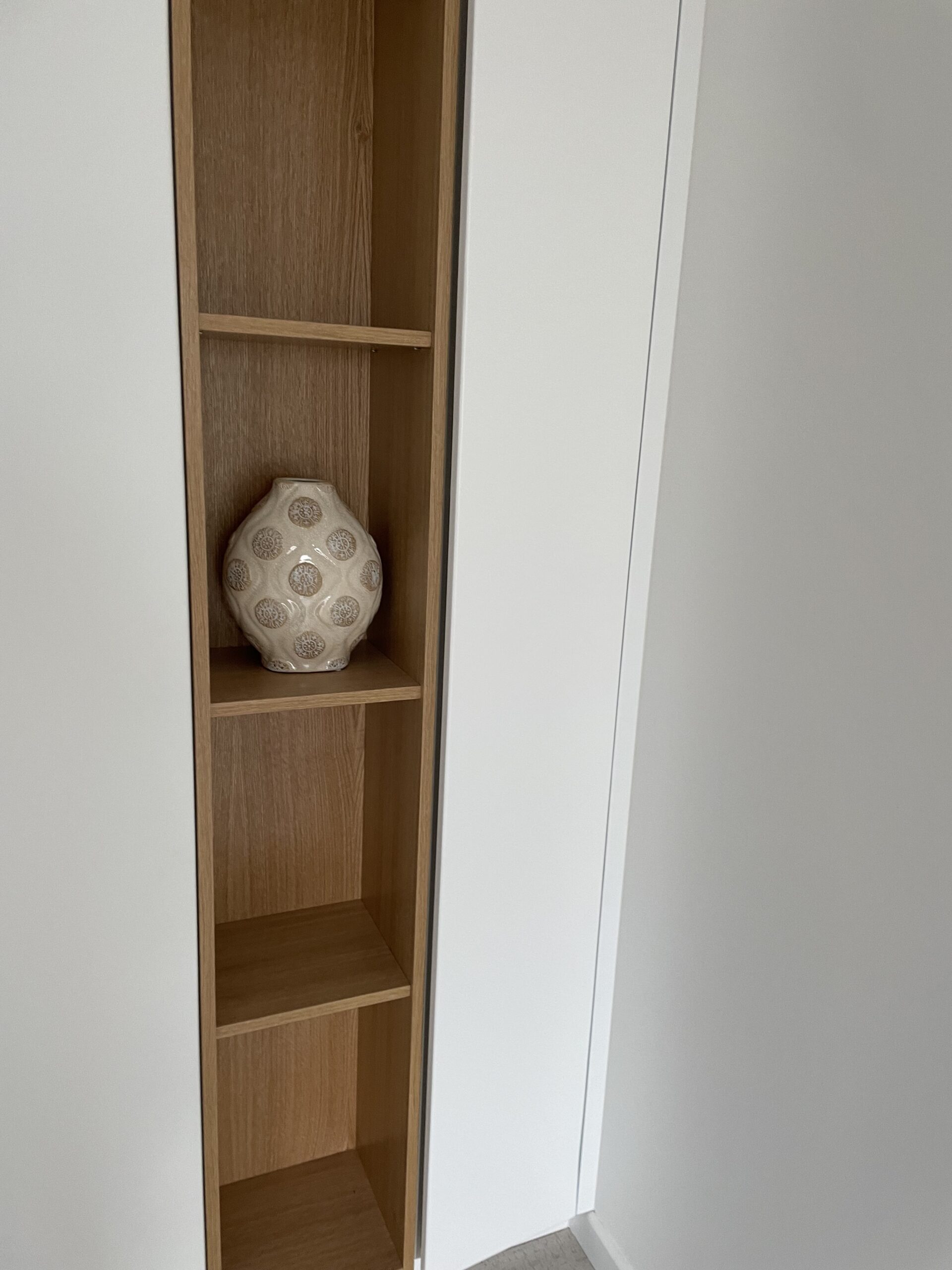 Étagère murale encastrée en bois clair avec un vase décoratif à motifs circulaires.