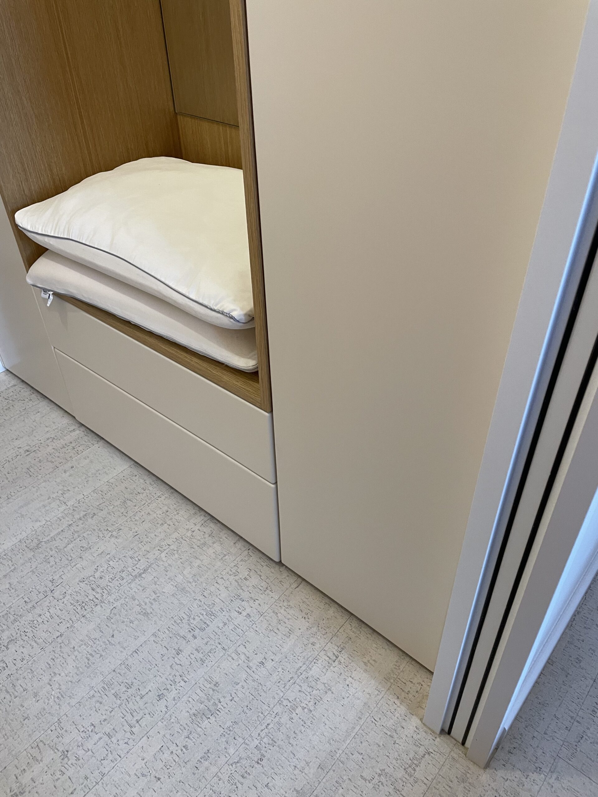 Étagère en bois d'un dressing moderne avec deux oreillers blancs empilés au-dessus de tiroirs beiges.